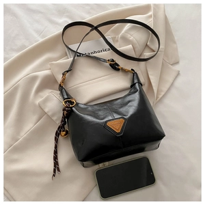 Detail of black leather dumpling bag with metal triangle logo on a neutral blazer background
