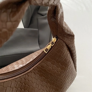 Brown woven embossed shoulder bag with gold-tone zipper on a gray blazer background