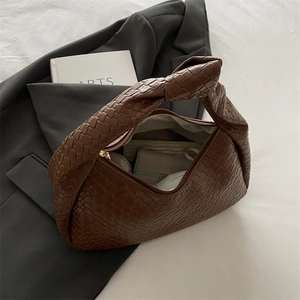 Brown woven leather underarm bag with a knotted handle on a grey suit jacket background