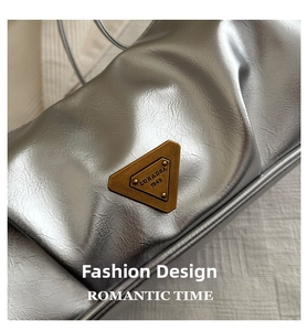 Nahaufnahme der silbernen Faltenstruktur und des bronzenen Metalllogos auf der Tasche