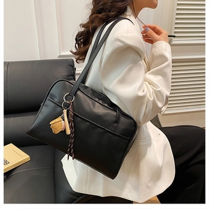 Detail of black PU leather tote bag with baseball pendant and front pocket detail