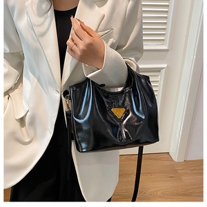 Dettaglio della borsa tote nera lucida con piastra a triangolo dorata su blazer