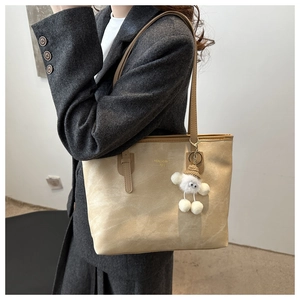 Detail of beige tote bag with gold brand text and a white plush lamb charm on strap