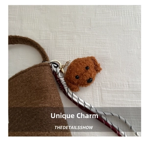Close-up of a brown plush teddy dog charm on a felt bag with golden spring clasp
