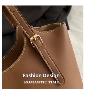 Detailed close-up of brown leather tote bag with gold buckle and white contrast stitching