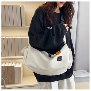 Detailed shot of white nylon messenger bag with orange pin and black strap in a library