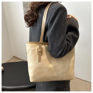 Detailed view of cream tote bag with brown shoulder strap worn by model in minimalist setting