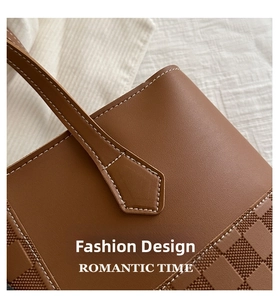 Detail of brown leather tote bag showing white contrast stitching and checkered pattern