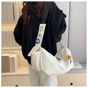 Detail view of white nylon messenger bag featuring stylish decorative badges on the strap
