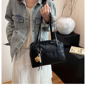 Close-up of a black matte leather tote bag with unique decorative biscuit charm pendant