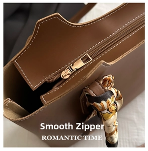 Detail view of smooth metal zipper and floral silk scarf on brown leather tote bag