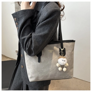 Detail of grey suede-textured tote bag with black leather straps and plush charm