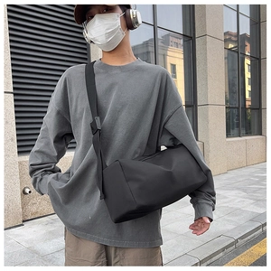 Détail d'un sac cylindrique en nylon noir avec bandoulière réglable porté par un homme