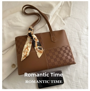 Detail of brown leather tote bag with checkered panel and scarf next to a phone