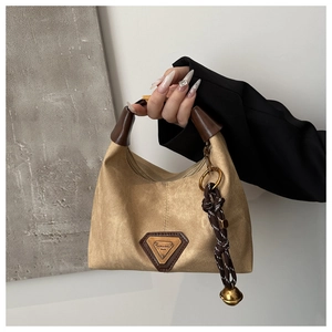 Detail of khaki canvas handbag featuring leather trim and golden bell pendant charm