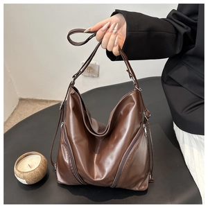 Detail of brown soft leather tote bag featuring side zipper accents and adjustable strap