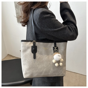 Detail of canvas tote bag with black leather straps and a cute white plush pendant