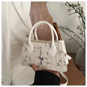 Close-up of woven cream handbag featuring floral embroidery and silver star buckle