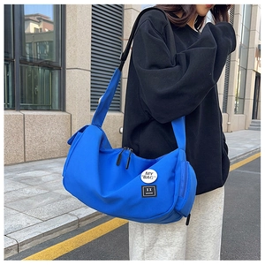 Outdoor shot of a royal blue nylon messenger bag with adjustable strap and badge details