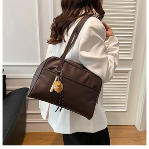 Detail of a large dark brown tote bag with baseball pendant worn with a white blazer
