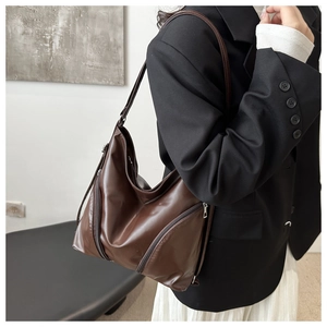 Detail of dark brown soft leather shoulder bag with side zipper on model in suit