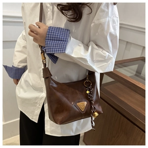 Detailed view of brown leather crossbody bag with iconic metal triangle plate and charms