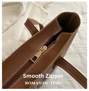 Detail of contrast stitching and smooth gold-tone zipper on brown faux leather tote bag