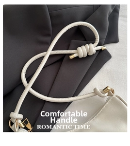 Detail of minimalist cream leather bag with knotted handle and gold metal hardware