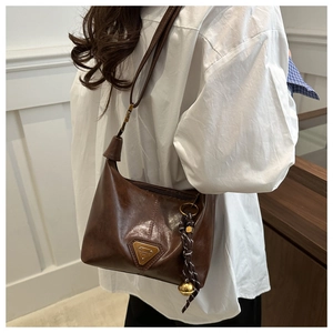 Detail of vintage brown dumpling bag with polished leather texture and woven pendant