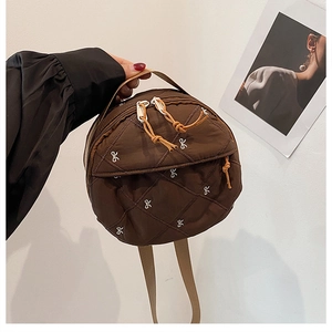 Detail of round dark brown quilted bag featuring white bow embroidery and dual zippers