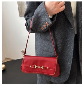 Detail of red leather shoulder bag with gold horsebit buckle against grey suit