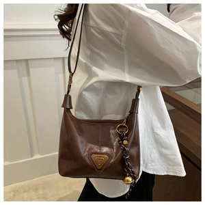 Detail of vintage brown leather bag with glossy finish and decorative bell charm pendant