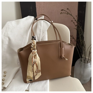 Detailed view of brown leather tote bag with silk scarf accent and gold hardware