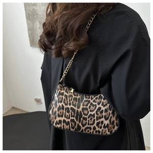 Close-up of leopard print underarm bag with gold chain strap worn by a model in black