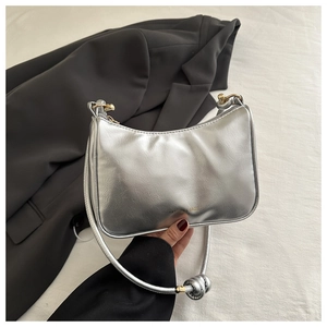 Detail of silver metallic baguette bag with golden metal sphere knot on the shoulder strap