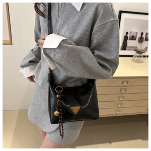 Detail of glossy black leather crossbody bag with gold triangular metal logo and charms