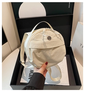 Close-up of beige round crossbody bag made of textured nylon with dual zippers and logo