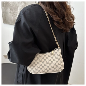 Detailed view of monogram shoulder bag with chain strap worn on a black coat