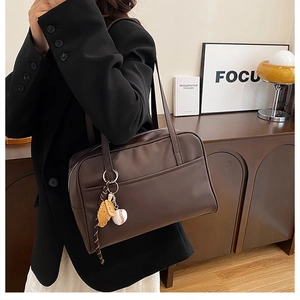 Close-up of a dark brown leather tote bag featuring a decorative baseball-themed pendant