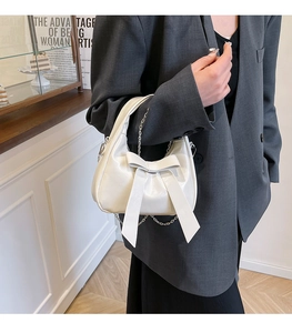 Detail of white bow handbag featuring glossy finish and elegant silver metal chain