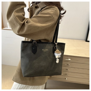 Detail of dark grey tote bag with gold logo, slim straps, and plush ball charm accessory