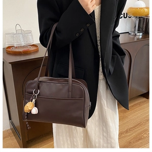 Detail of dark brown leather tote bag with unique baseball glove charm on shoulder strap