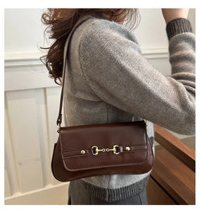 Detail of a dark brown leather baguette bag with a golden horsebit metal buckle ornament