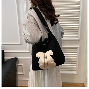 Detail of black corduroy tote bag featuring a large cream puppy plush patch and drawstring