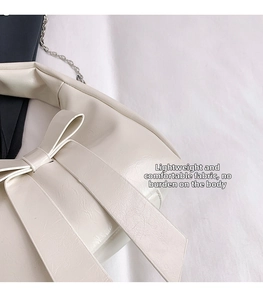 Close-up of a cream white shoulder bag with a large bow detail and silver chain strap