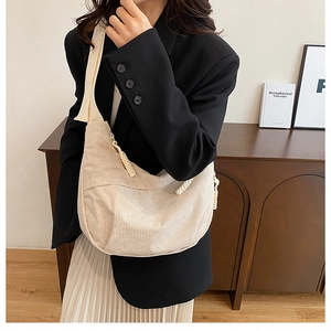 Close-up of beige corduroy crescent bag with textured stripes on model outfit