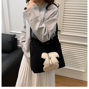 Detail view of black corduroy shoulder bag featuring a plush cream dog patch and drawstring