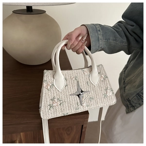 Detail of floral embroidery and star metal buckle on woven cream handbag