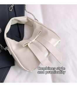 Detail of cream white faux leather shoulder bag featuring a large decorative bow and chain