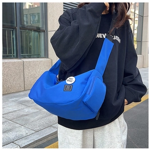Detail of Klein blue nylon messenger bag with side zip pocket and decorative badges